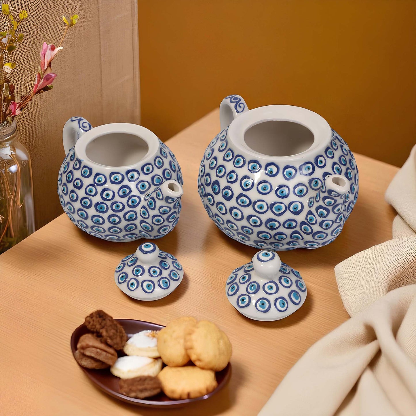 Two ceramic teapots with blue and white patterns on a wooden surface with cookies and a plate.