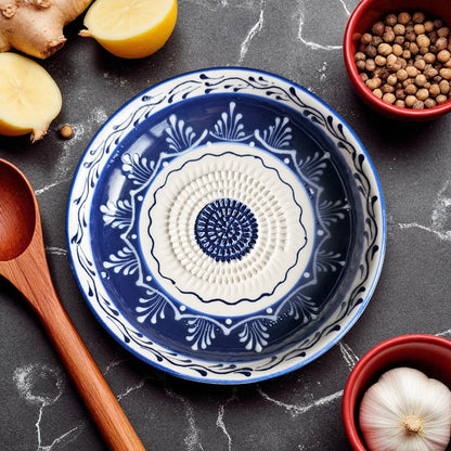 Blue and white decorative garlic grater bowl on a dark surface with kitchen items around