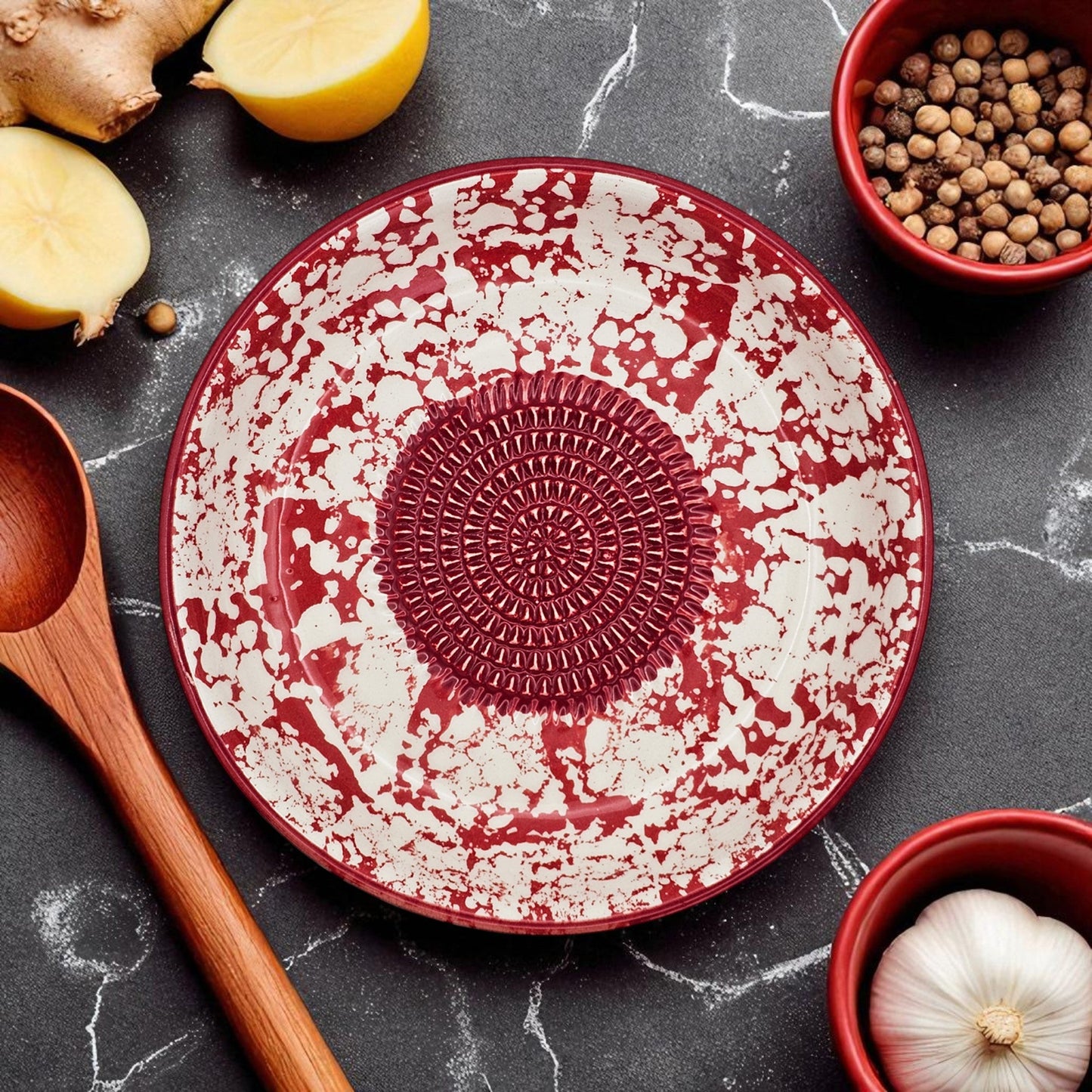 Red and white ceramic garlic grater bowl with textured center on a dark marble surface with kitchen items.