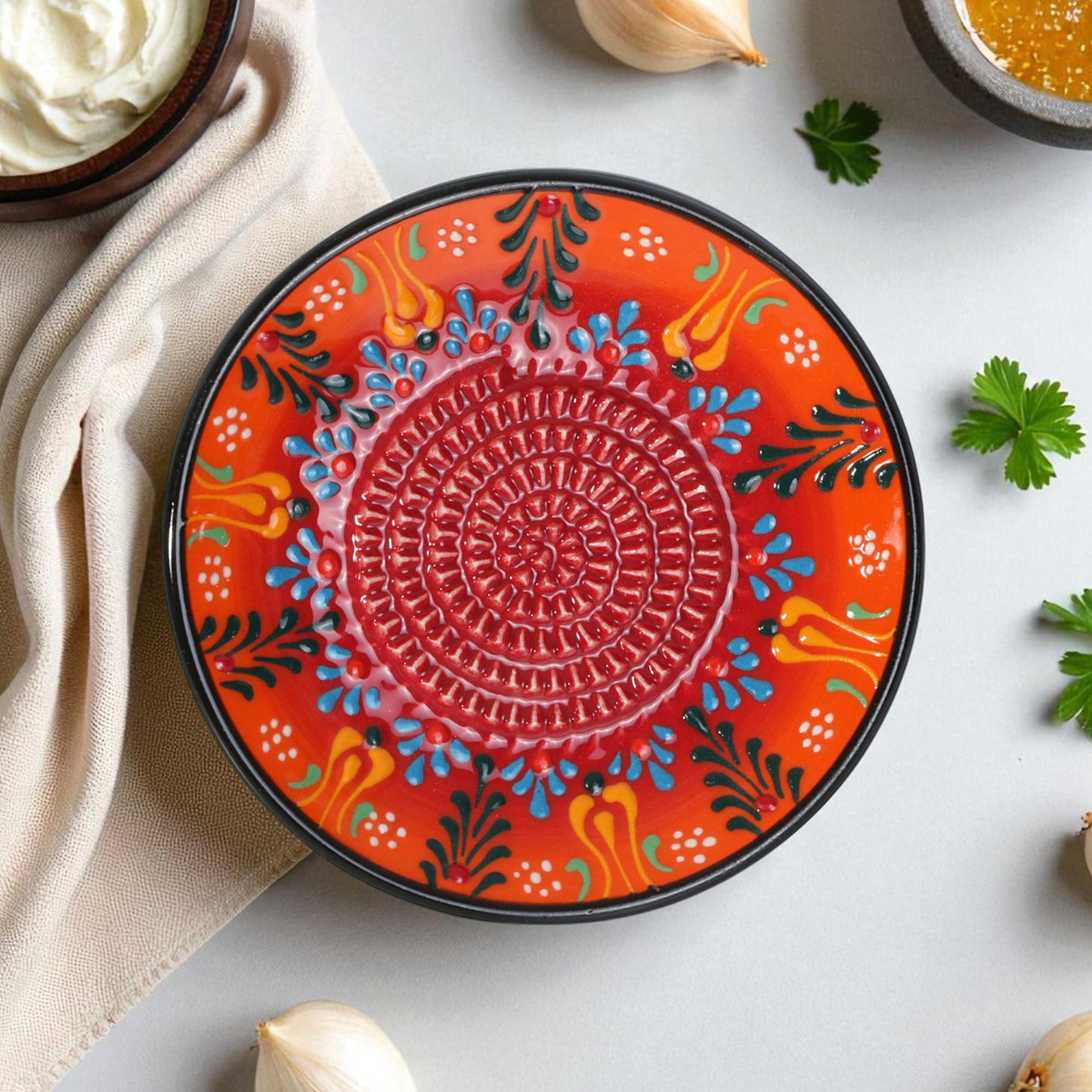 Decorative ceramic garlic grater plate with colorful patterns on a light surface with ingredients.