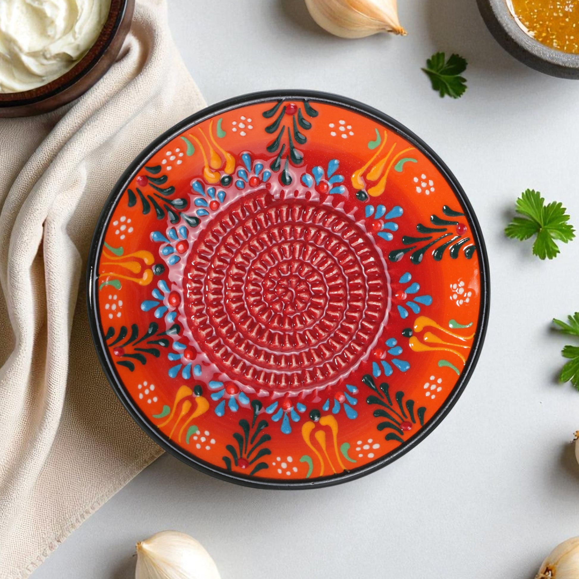 Decorative ceramic garlic grater plate with colorful patterns on a light surface with ingredients.
