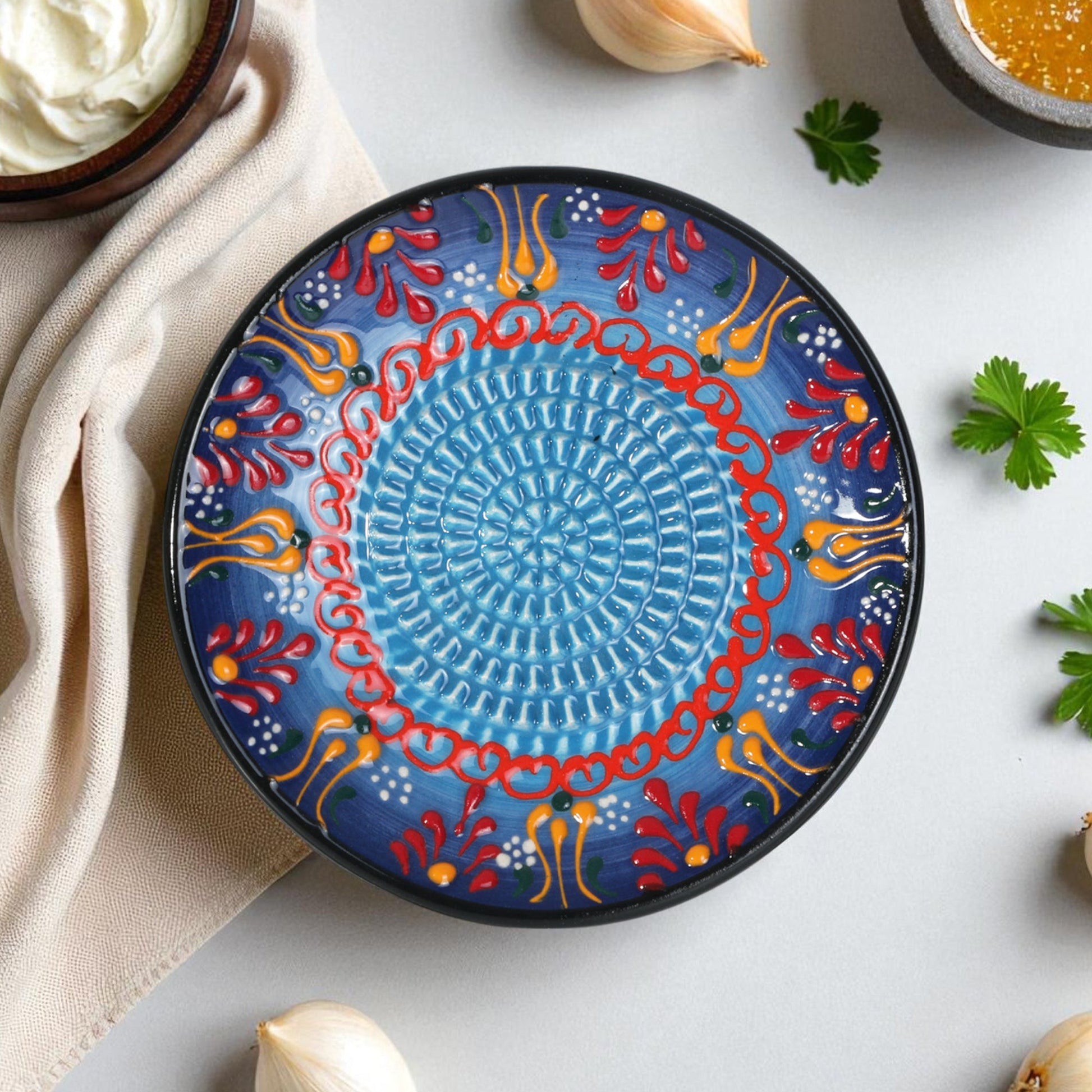 Decorative ceramic garlic grater plate with colorful patterns on a light surface with ingredients.