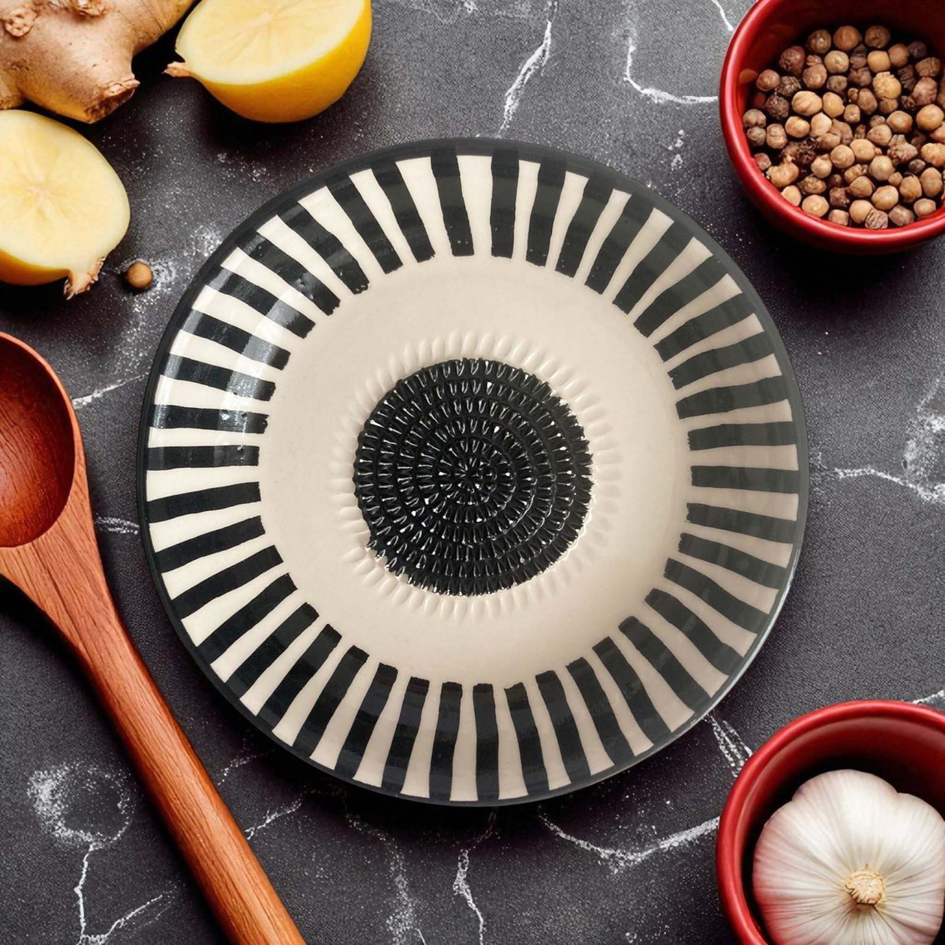 Decorative garlic grater bowl with black and white striped design on a dark surface with kitchen items.