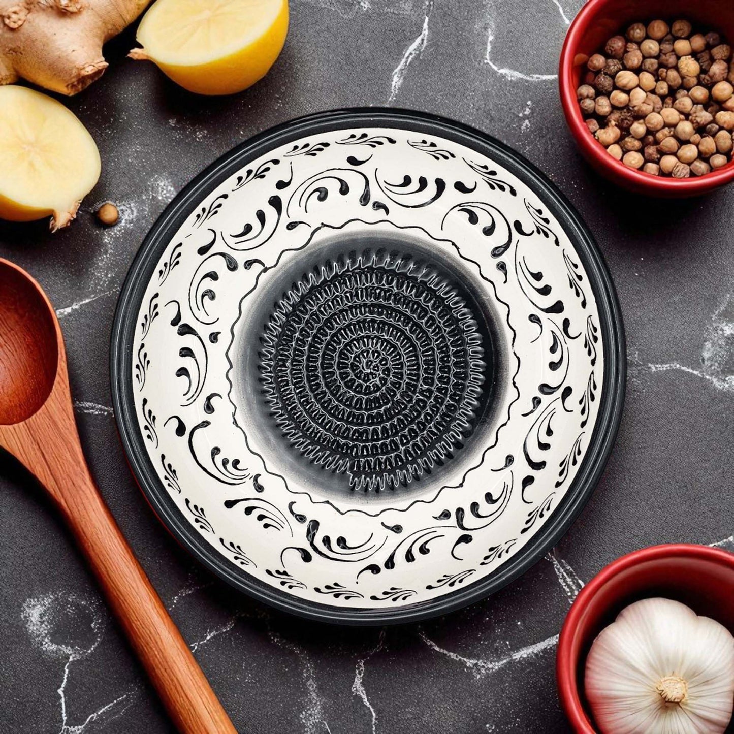 Decorative ceramic garlic grater bowl with black and white pattern on a dark surface with kitchen items.