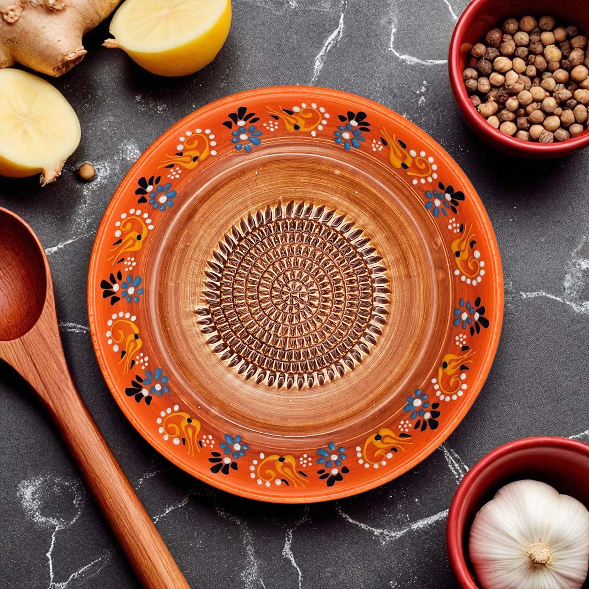 Decorative ceramic garlic grater bowl with floral patterns on a dark surface with kitchen items.