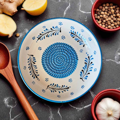 Decorative ceramic garlic grater bowl with blue and black patterns on a dark surface with kitchen items.