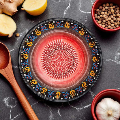 Decorative black garlic grater bowl with colorful patterns on a dark surface with kitchen items.