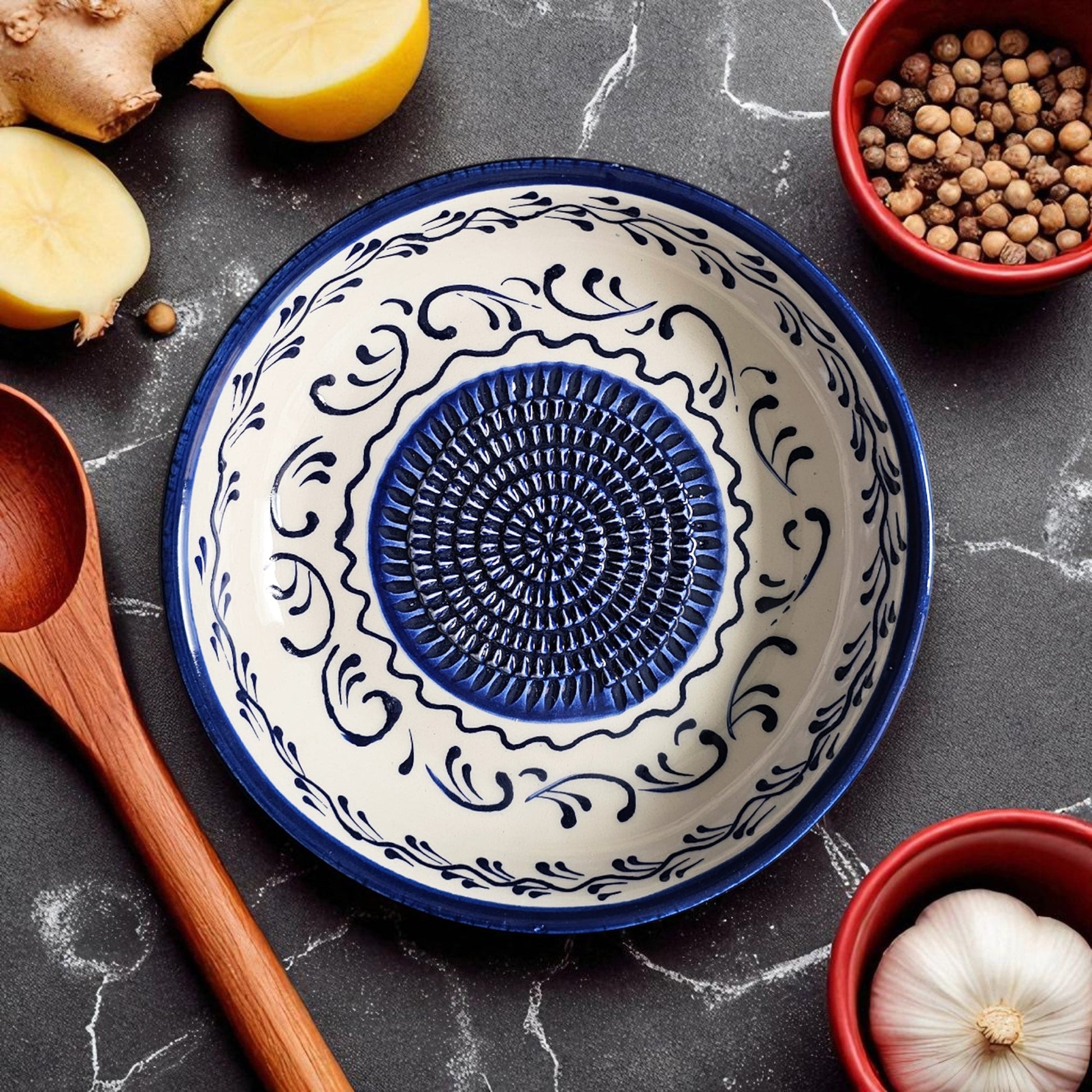 Decorative ceramic garlic grater bowl with blue and white pattern on a dark surface with kitchen items.