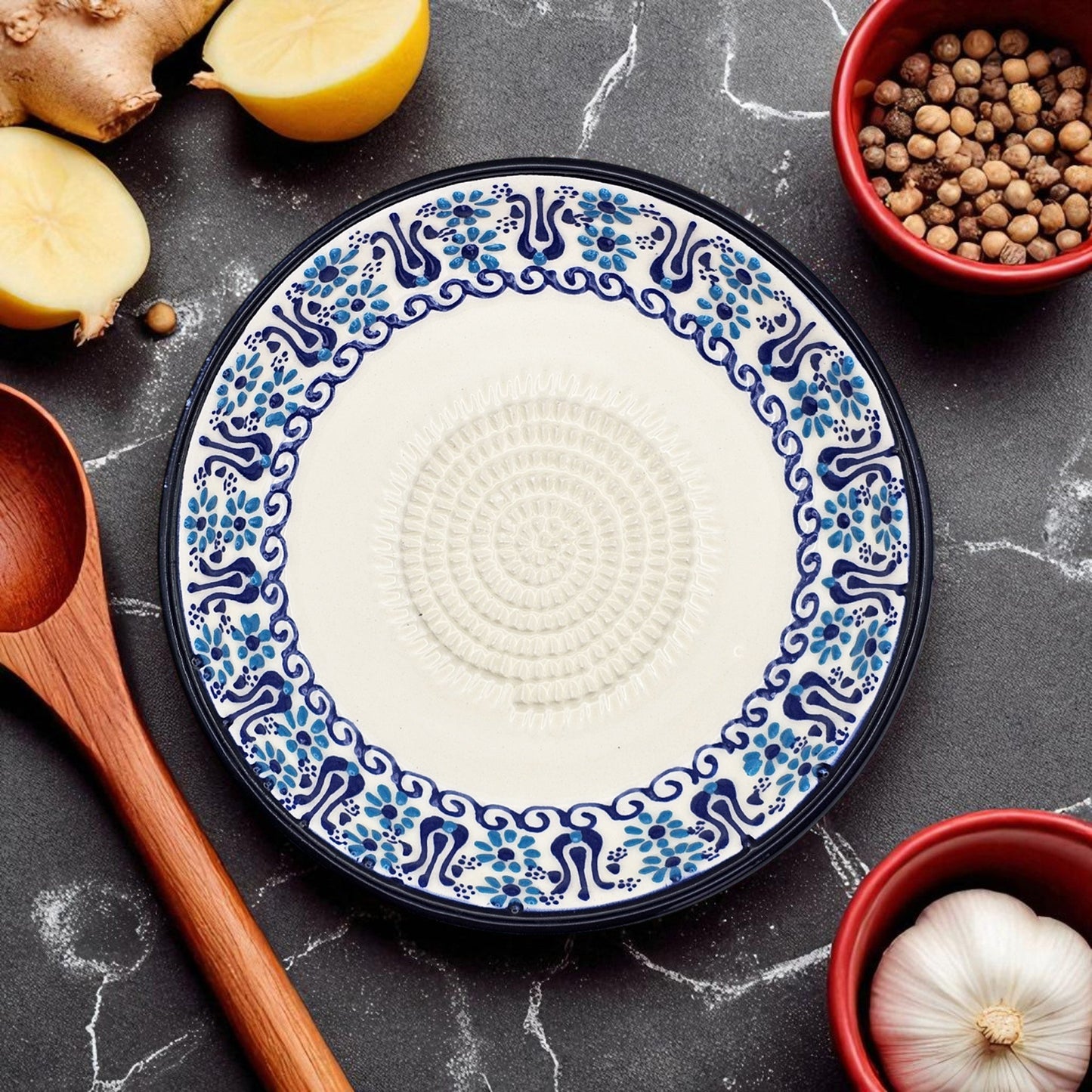 Decorative garlic grater plate with blue and white pattern on a dark surface with ingredients