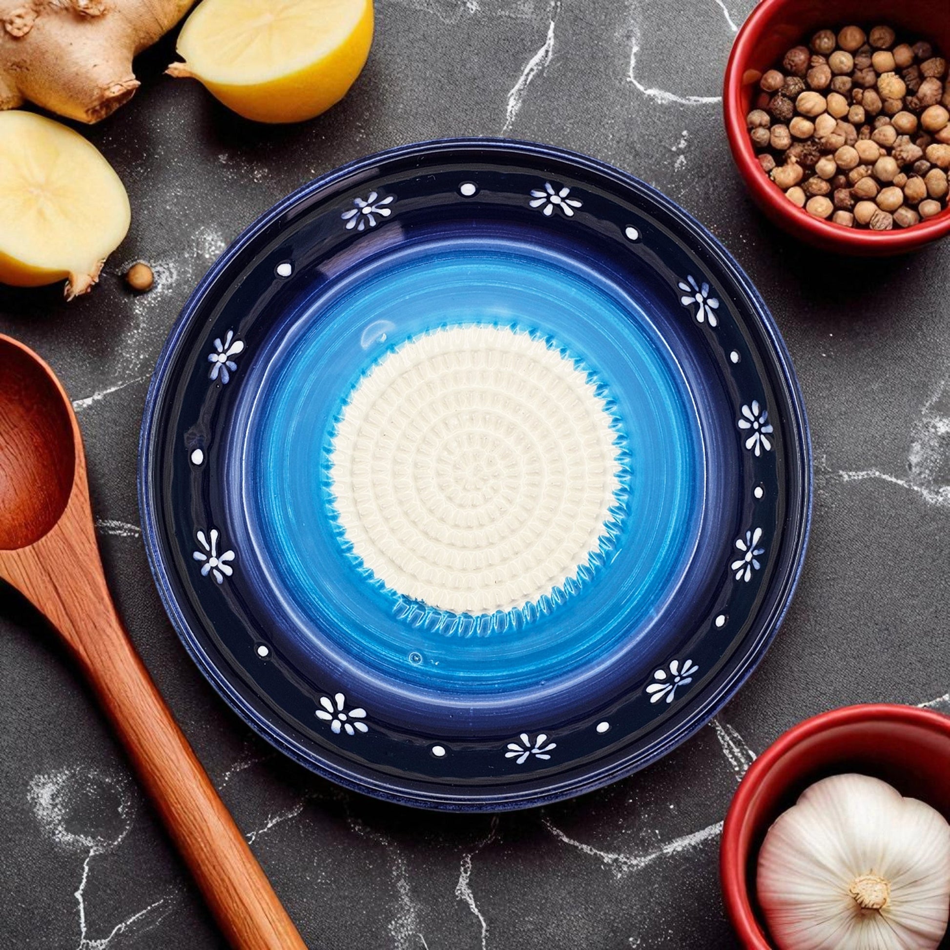 Blue ceramic garlic grater bowl with white center on a dark surface with kitchen items