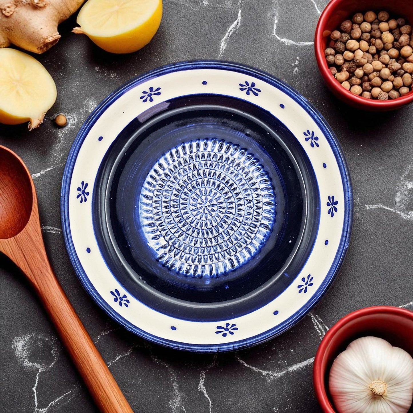 Blue ceramic garlic grater bowl with decorative pattern on a dark surface with kitchen items.