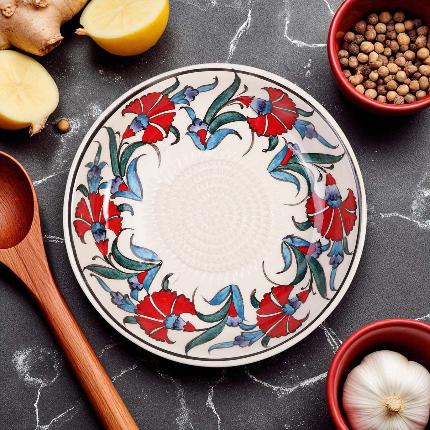 Decorative ceramic garlic grater bowl with floral patterns on a dark surface with kitchen items.