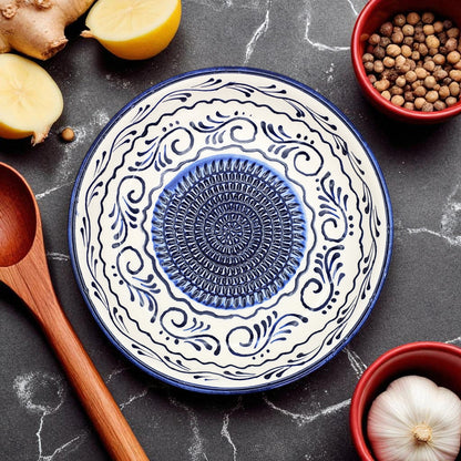 Decorative ceramic garlic grater bowl with blue center and white patterns on a dark surface with kitchen items.