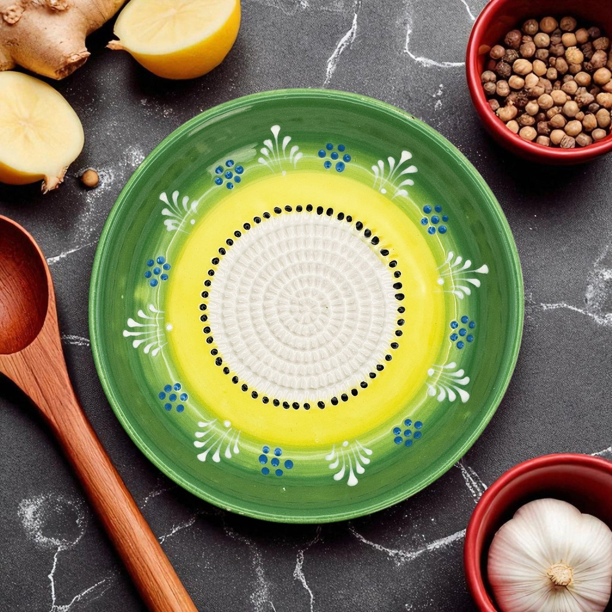 Decorative ceramic garlic grater bowl with green rim and yellow center on a dark surface with kitchen items.