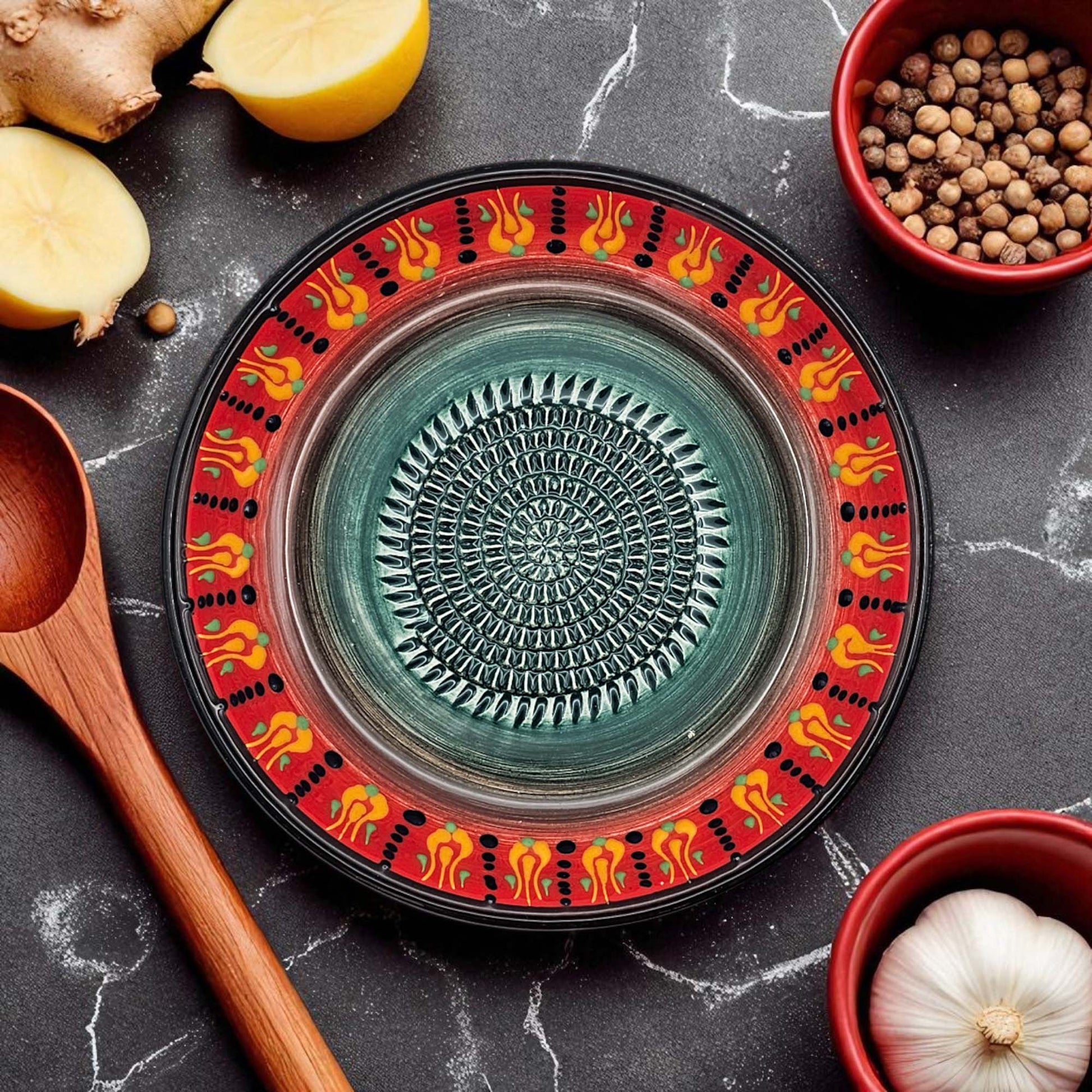 Decorative ceramic garlic grater bowl with colorful, surrounded by kitchen ingredients on a dark surface