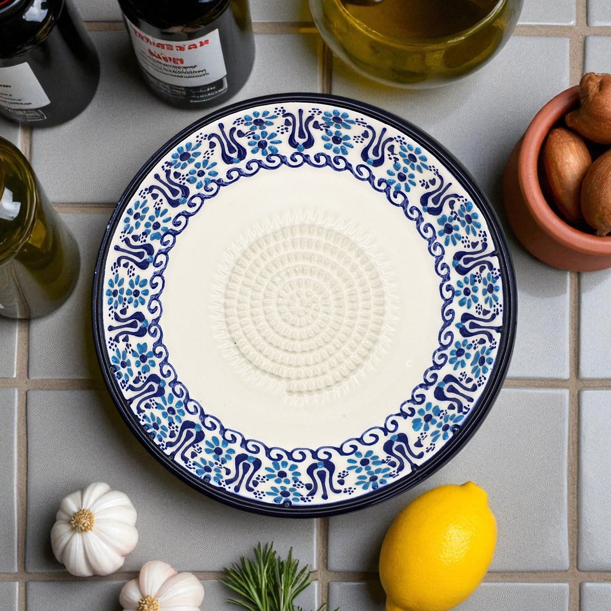 Decorative garlic grater plate with blue and white pattern on a tiled surface with lemons and garlic.