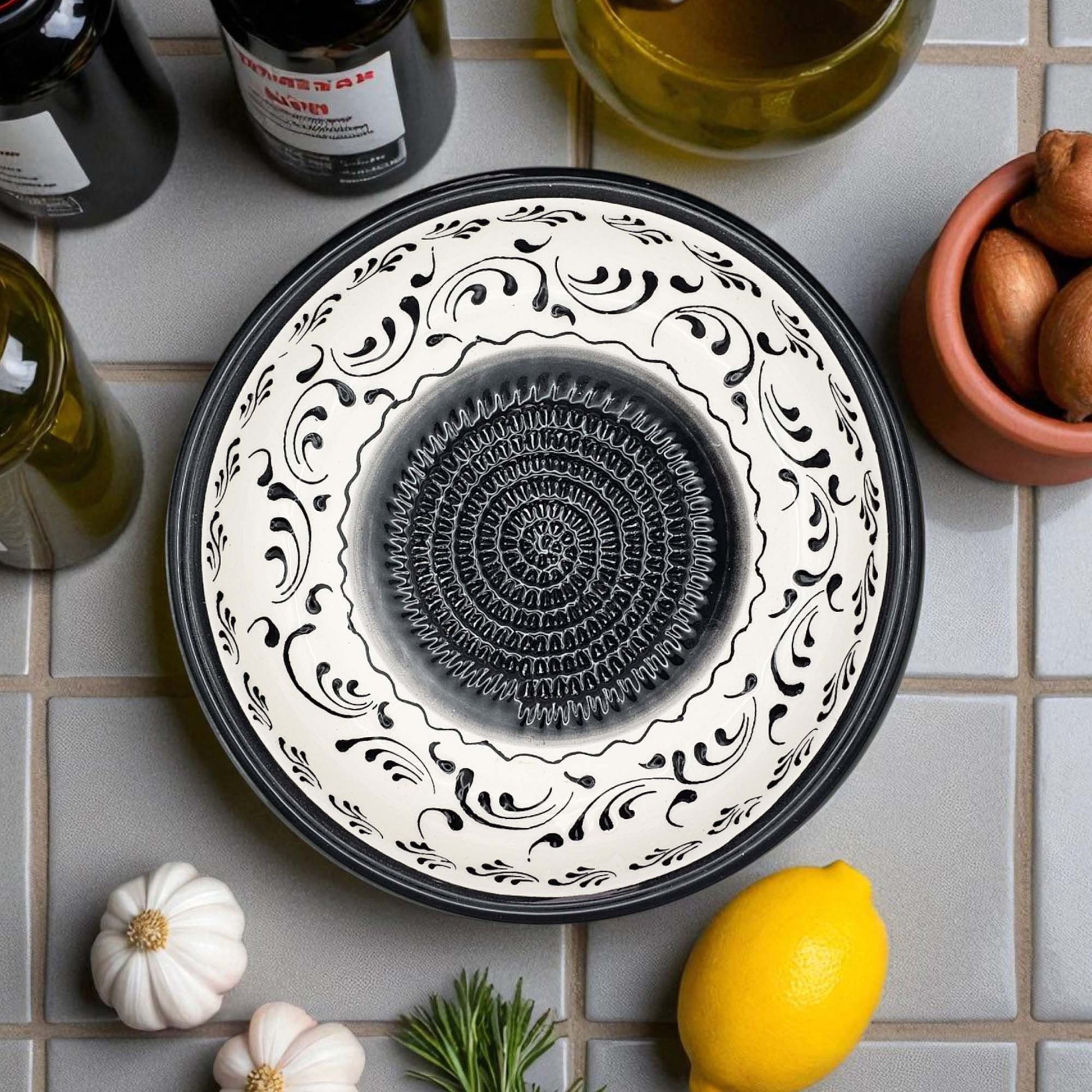 Decorative ceramic grater bowl with black and white pattern on a tiled surface with lemons and garlic.