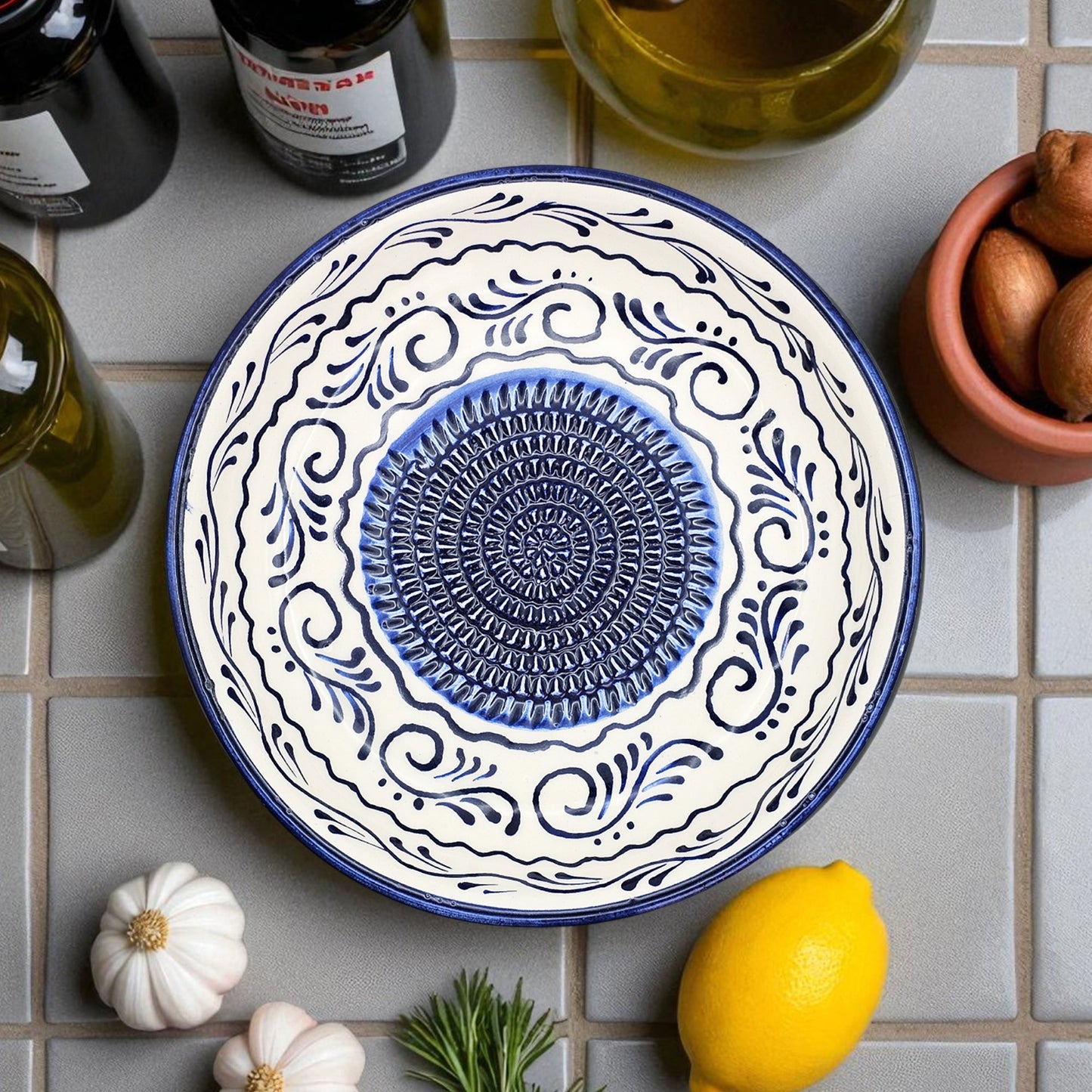 Decorative blue and white garlic grater bowl on a tiled surface with lemons and herbs.
