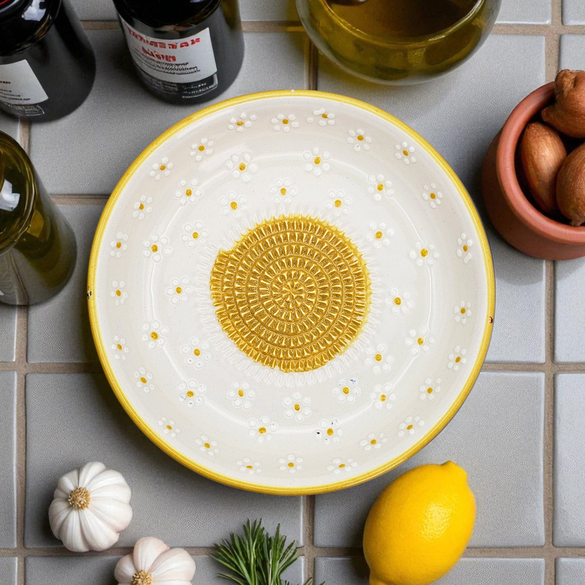 Decorative garlic grater bowl with yellow center and white rim on a tiled surface with lemons and garlic.