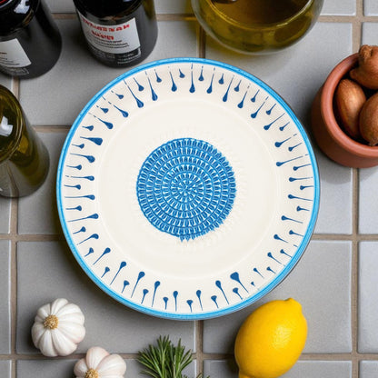 Decorative garlic grater bowl with blue and white pattern on a tiled surface with lemons and herbs.