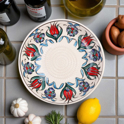 Decorative ceramic garlic grater bowl with floral patterns on a tiled surface with ingredients.