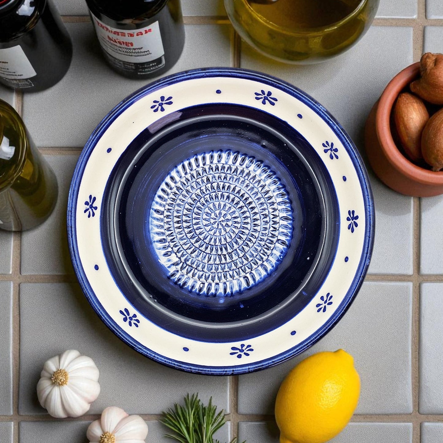 Blue ceramic garlic grater bowl with decorative pattern on a tiled surface with ingredients.