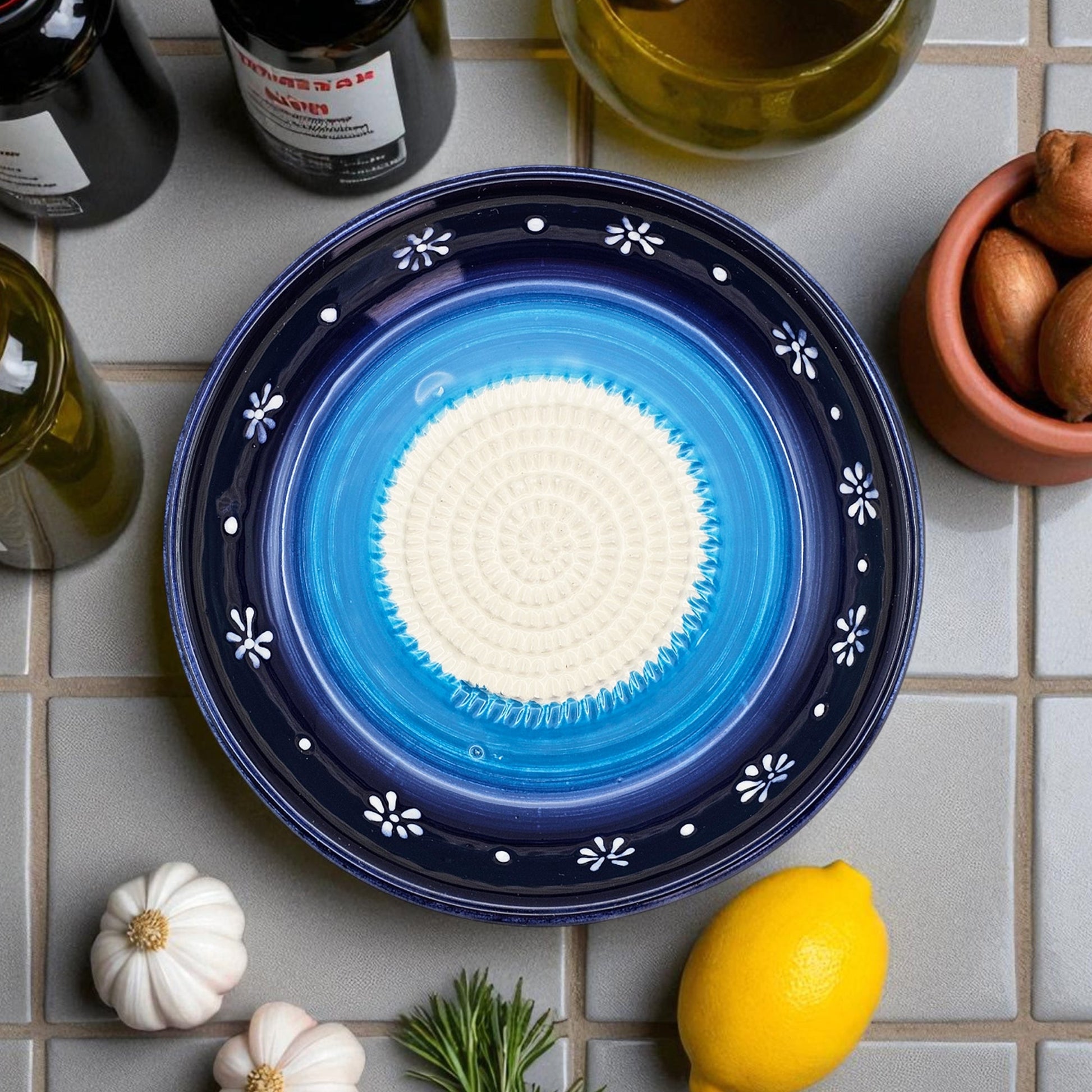 Blue ceramic garlic grater bowl with white center on a tiled surface with ingredients around