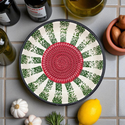 Decorative garlic grater bowl with a red center and green and white pattern on a tiled surface with lemons and herbs.