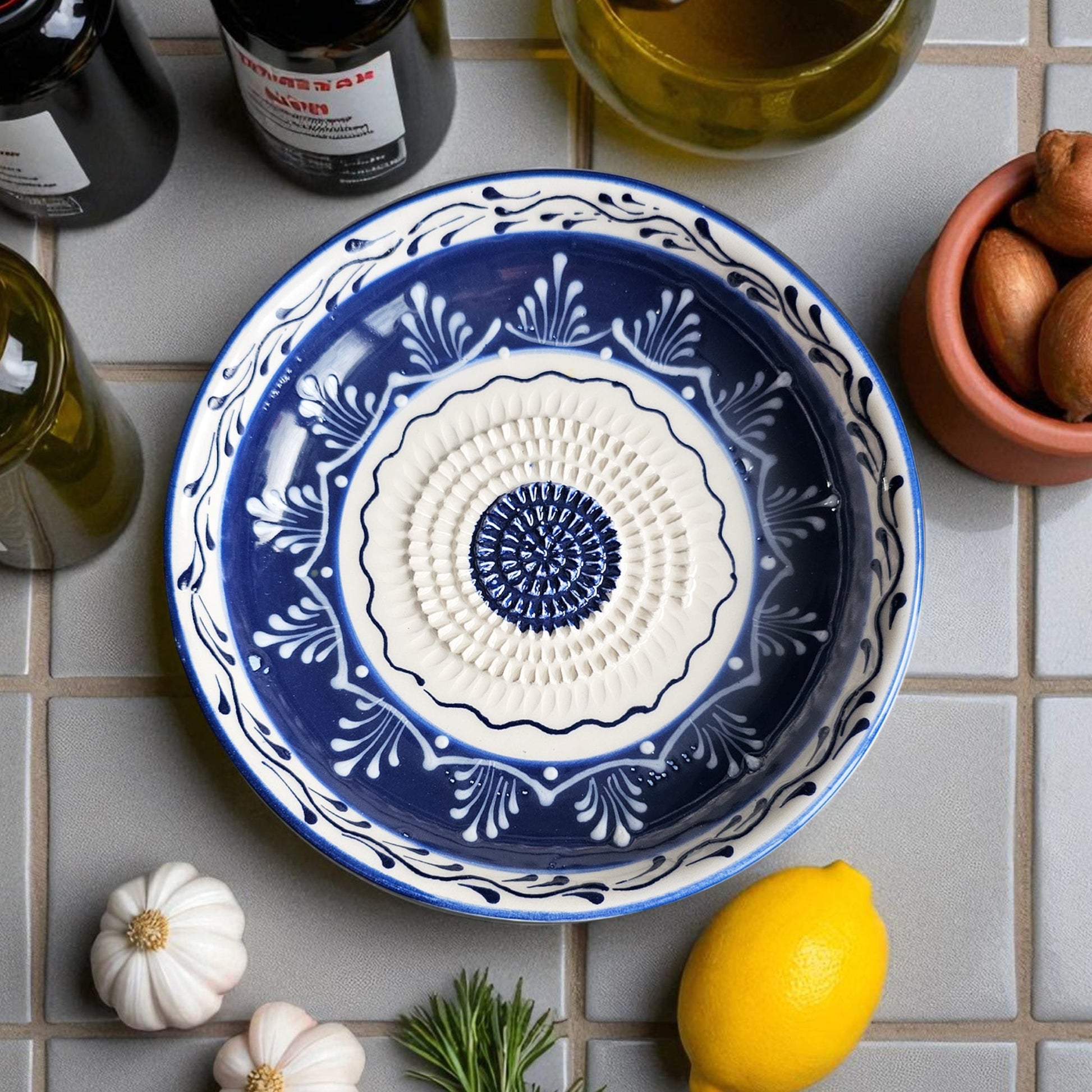 Decorative blue and white garlic grater bowl on a tiled surface with lemons and herbs.