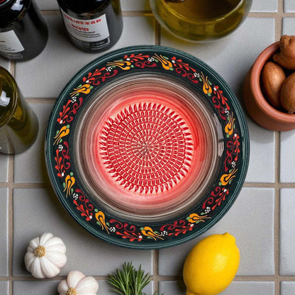 Decorative garlic grater bowl with floral patterns on a tiled surface with ingredients.
