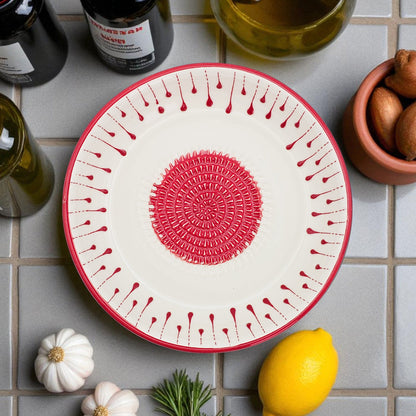 Decorative garlic grater bowl with red patterns on a tiled surface with lemons and bottles.
