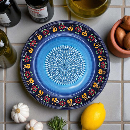 Decorative blue garlic grater bowl with colorful patterns on a tiled surface with ingredients.