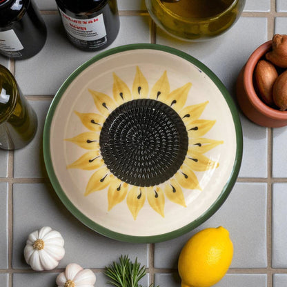 Ceramic garlic grater bowl with sunflower design on a tiled surface with ingredients.