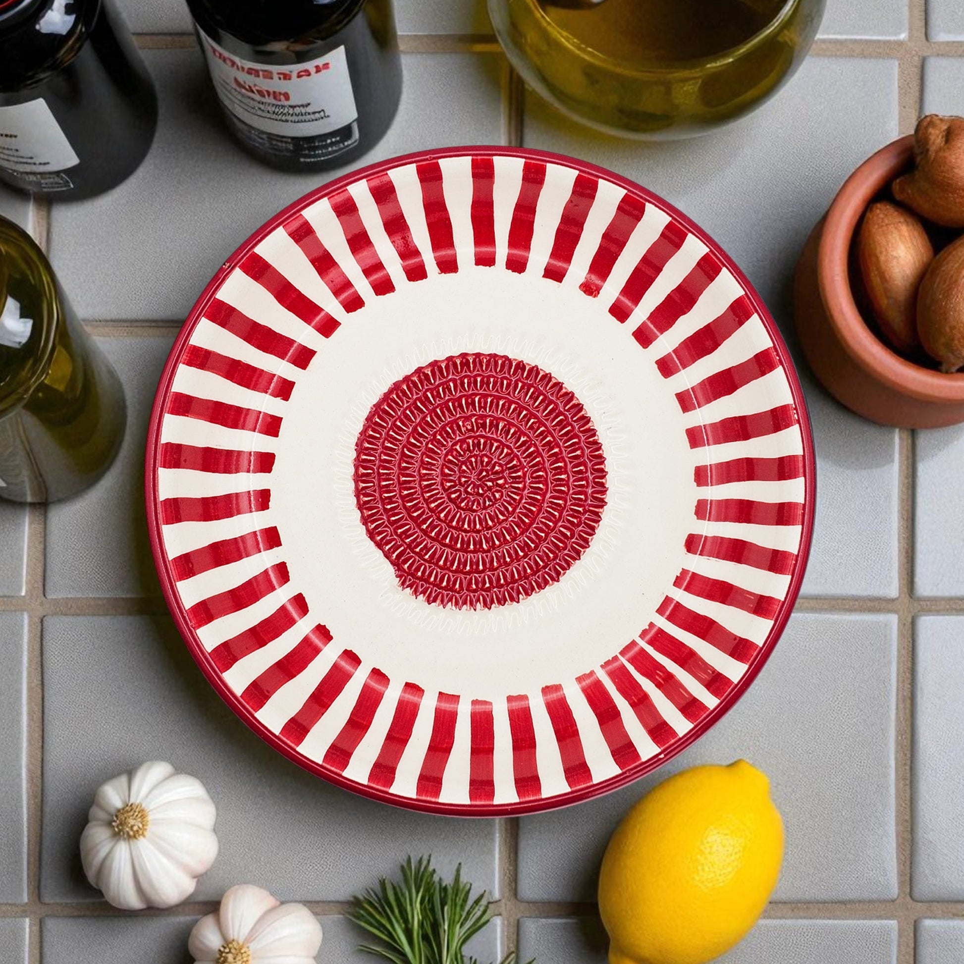 Red and white striped ceramic garlic grater bowl on a tiled surface with lemons and herbs.
