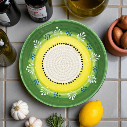 Decorative ceramic garlic grater bowl with green rim and yellow center on a tiled surface with ingredients.