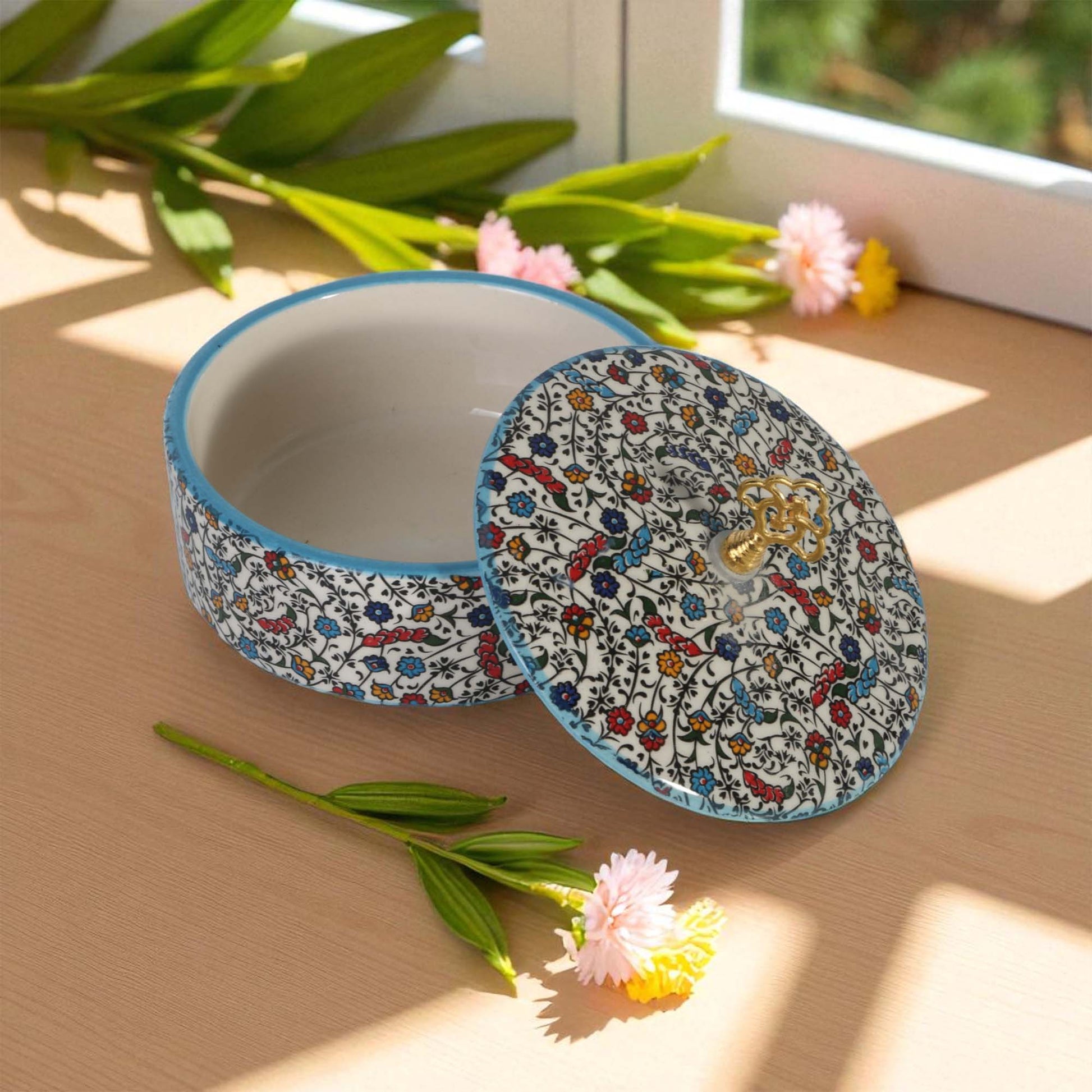 Decorative sugar bowl with floral pattern on a wooden surface with flowers and leaves.