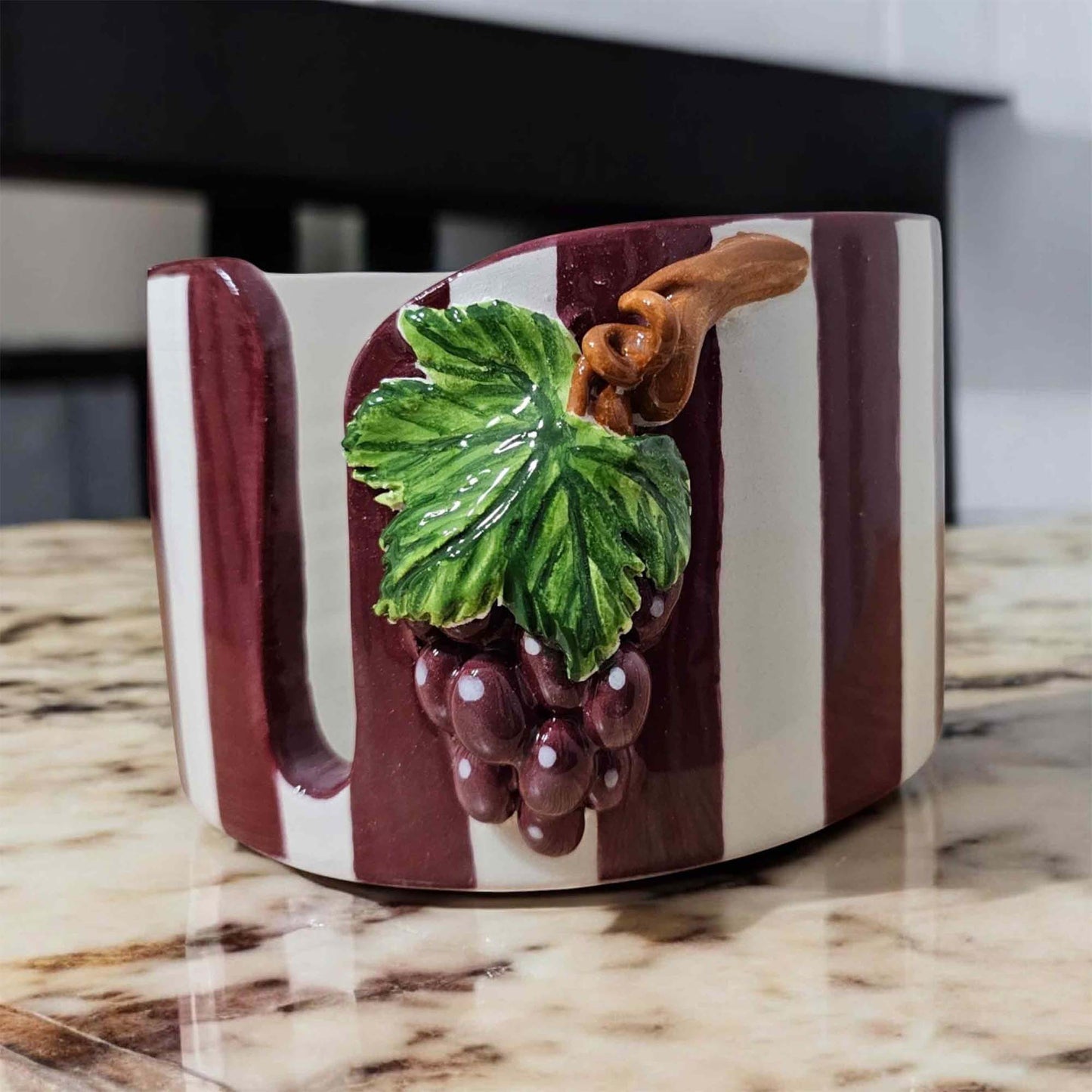Decorative paper towel holder with grape design on a marble surface