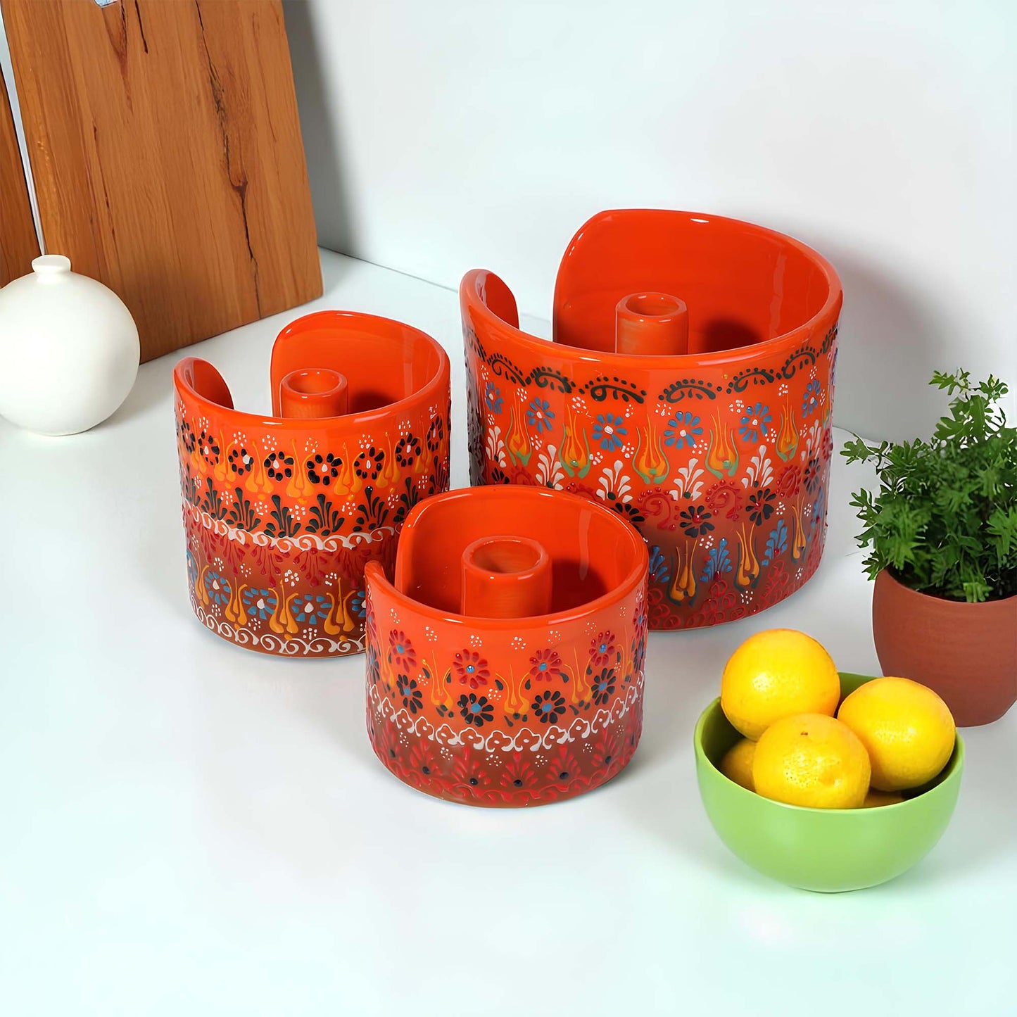 Set of orange ceramic paper towel holder with floral patterns on a white surface, accompanied by a green bowl with lemons.