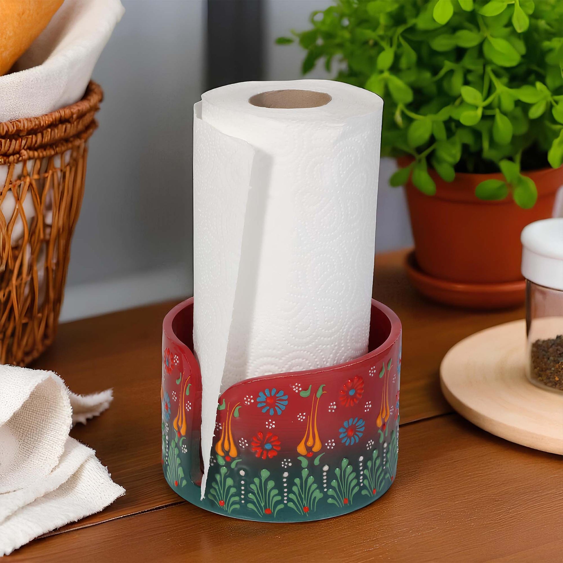 Decorative paper towel holder with a roll of paper towels on a wooden surface with a plant in the background.