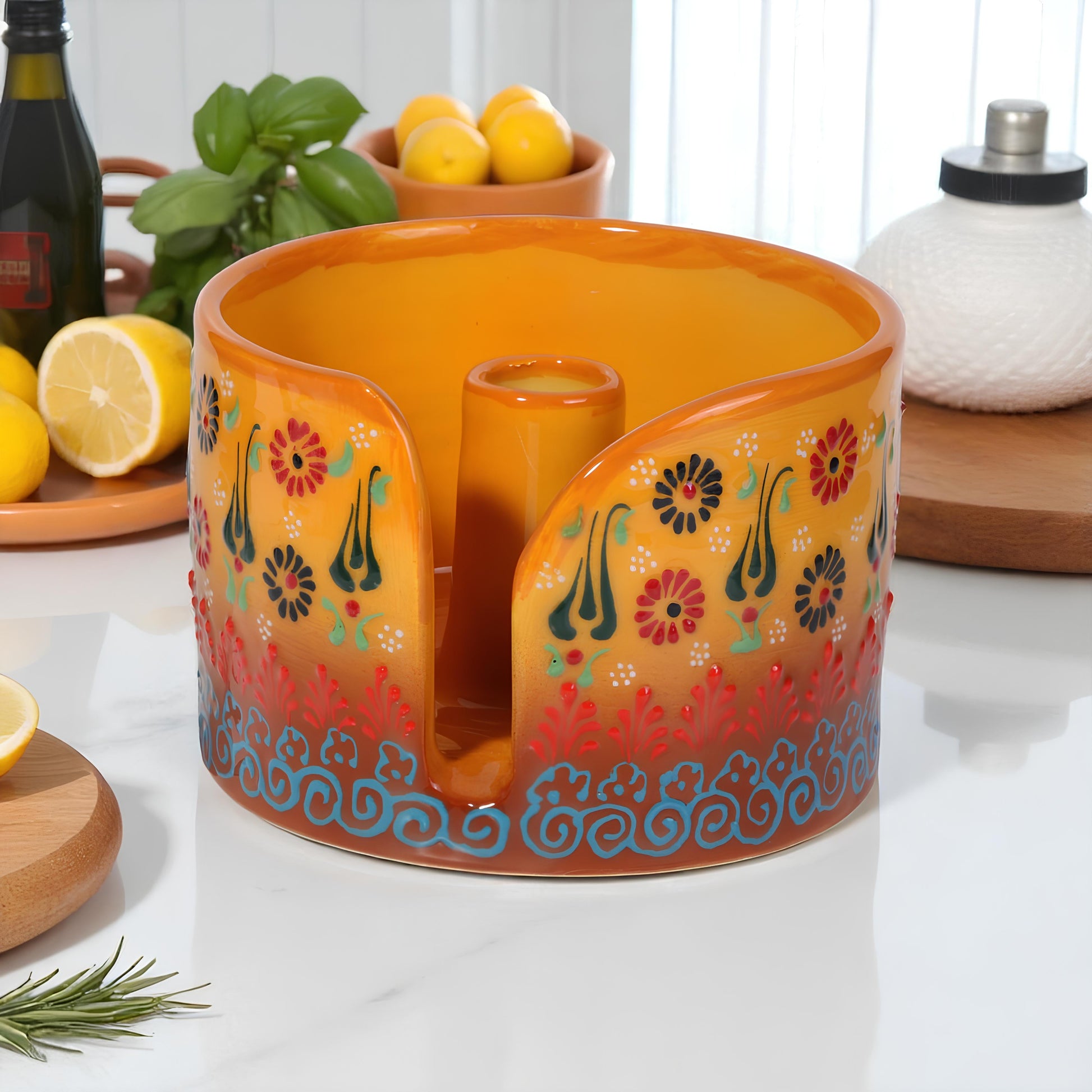 Decorative ceramic paper towel holder with floral patterns on a table with lemons and herbs.