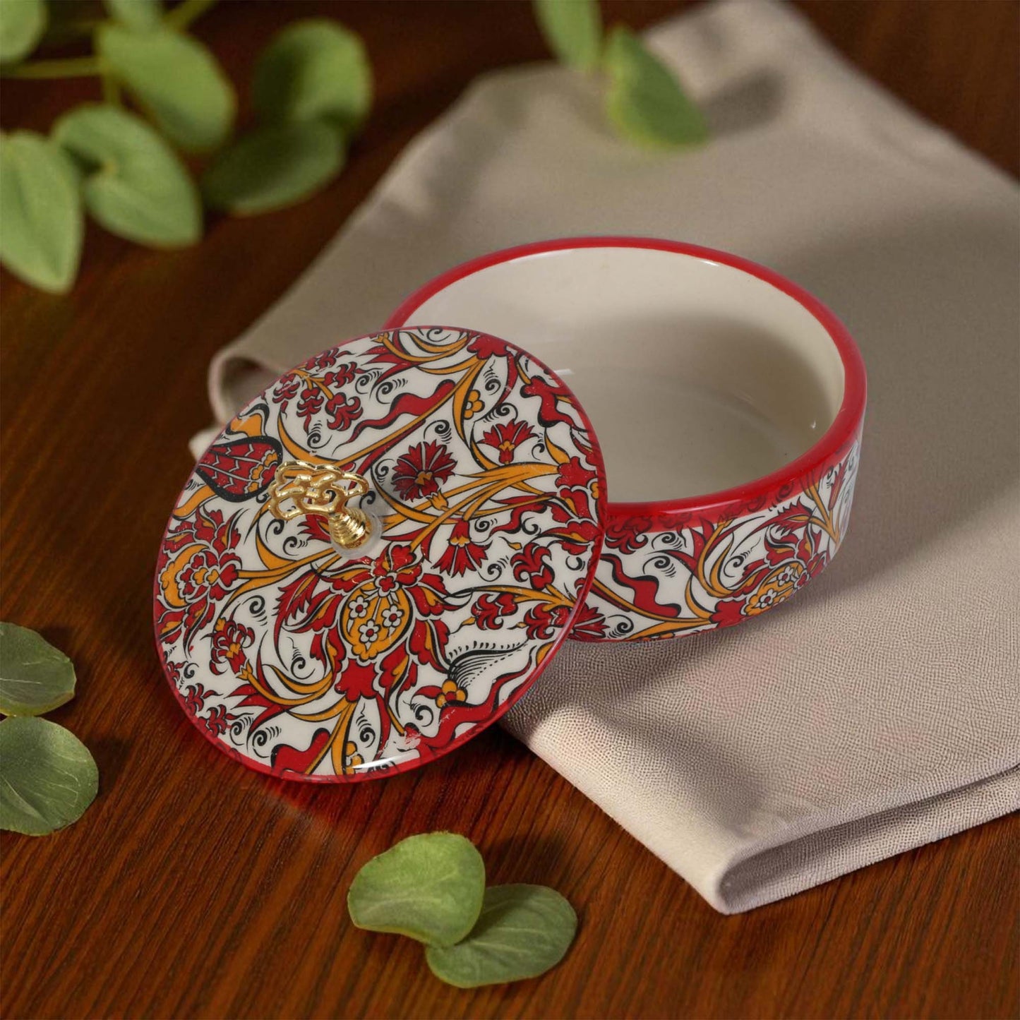Decorative ceramic sugar bowl with intricate patterns on a wooden surface with green leaves.