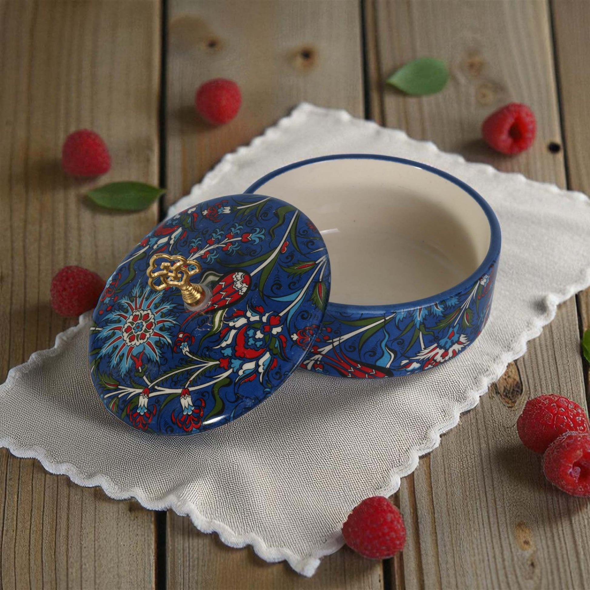 Decorative ceramic sugar bowl with floral design on a wooden surface with raspberries.