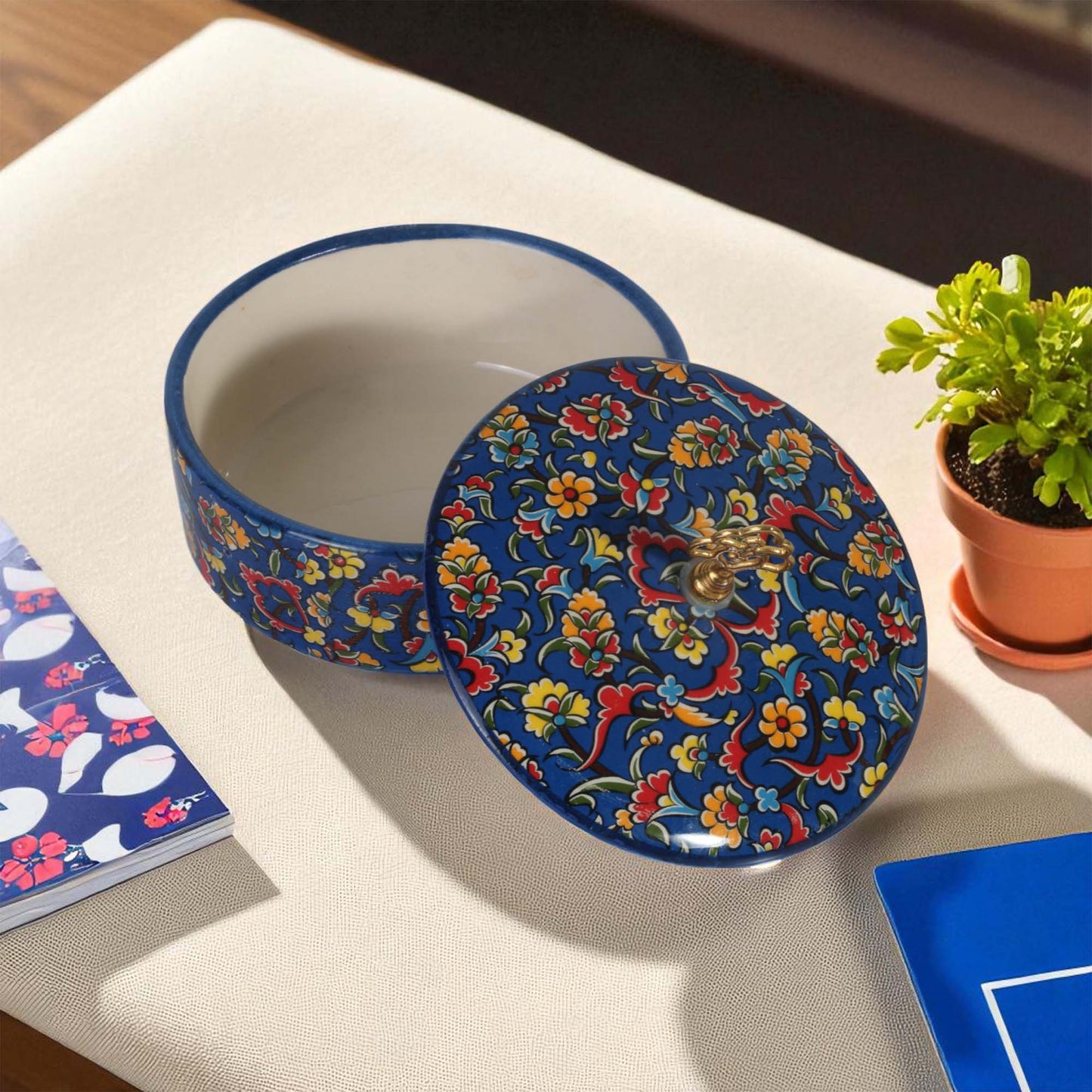 Decorative sugar bowl with floral design on a table with a plant and notebook.