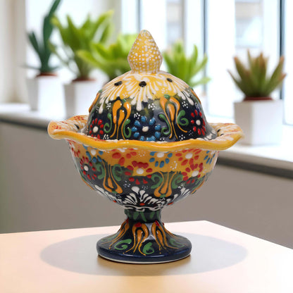 Colorful ceramic sugar bowl with lid on a table, plants in the background