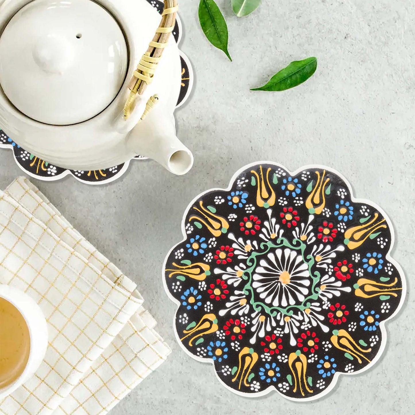 Decorative mandala trivet on a table with a teapot and cup.