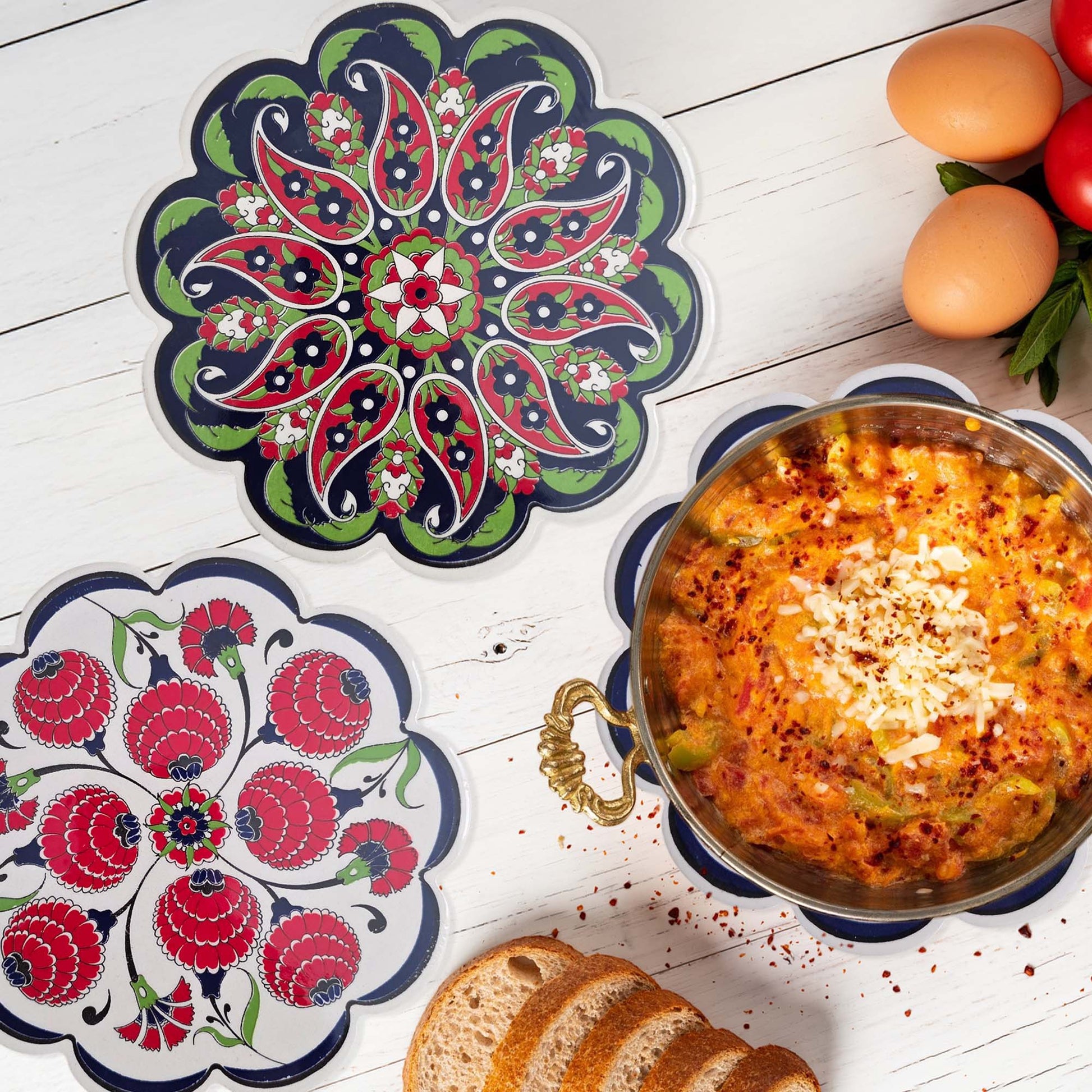 Decorative trivets with floral patterns on a wooden surface with food items.