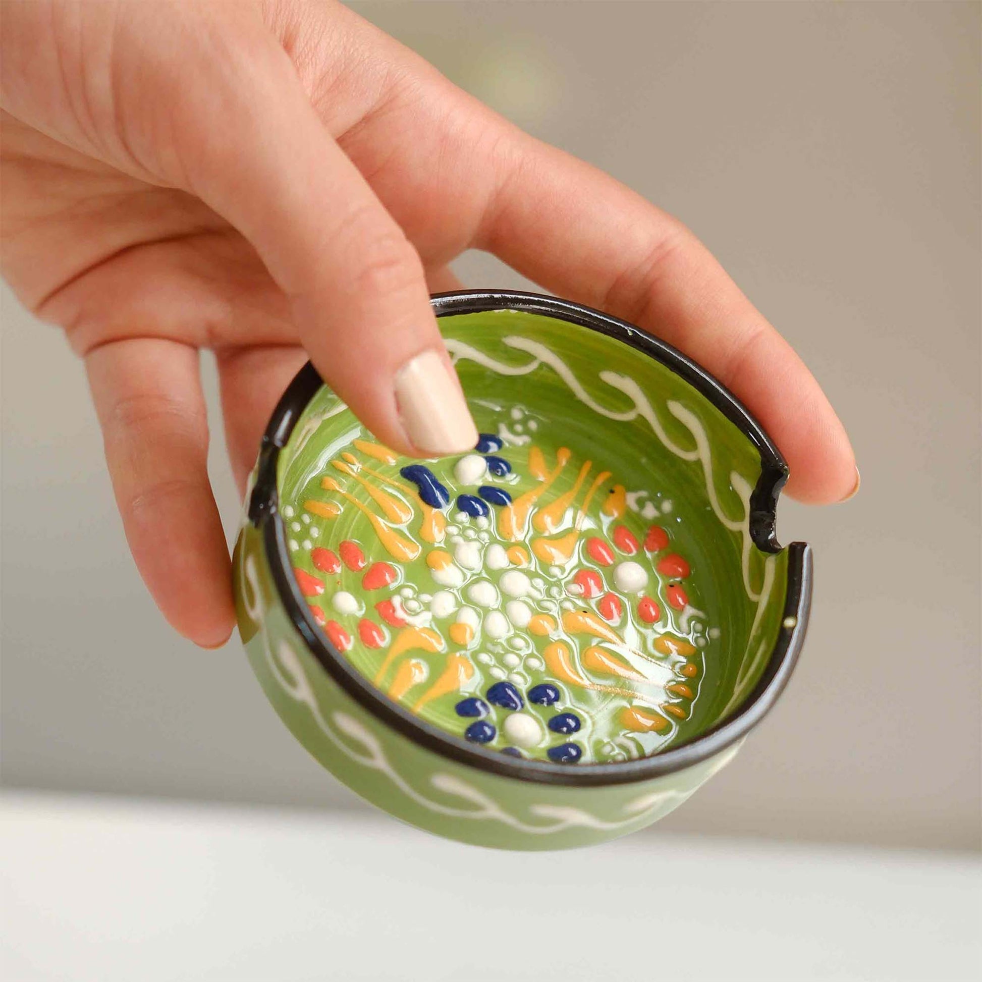 Hand holding a green ceramic ashtray with colorful patterns on a neutral background