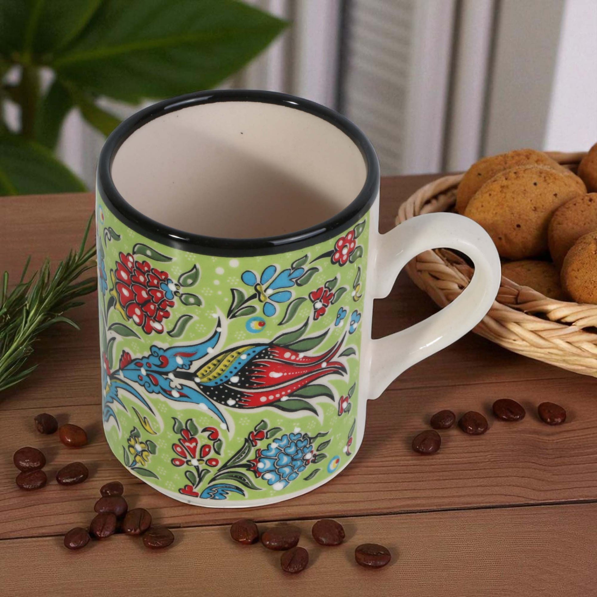 Colorful mug with floral and fish design on a wooden table with coffee beans and cookies.