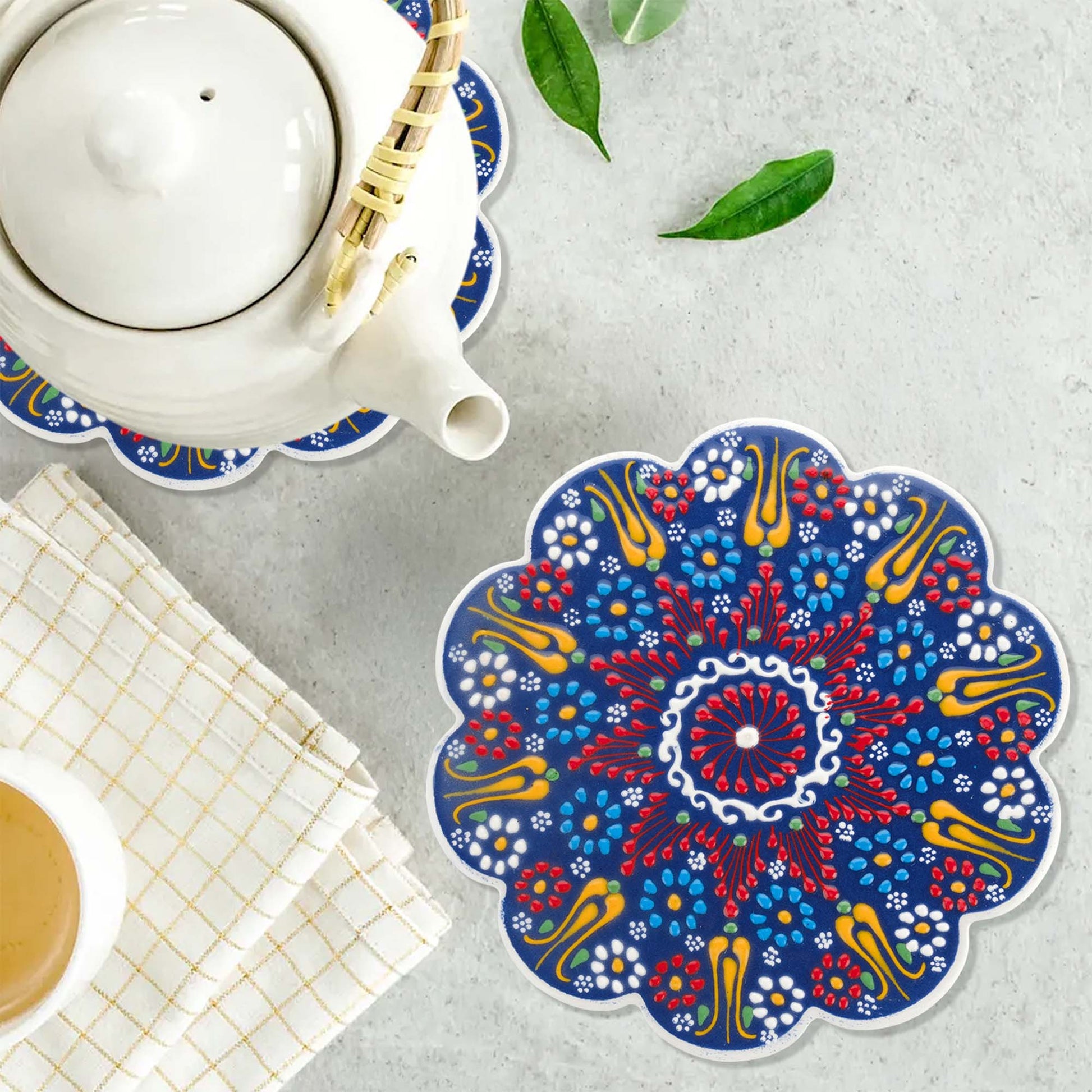 Colorful mandala trivet on a table with a teapot and cup.