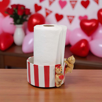 Striped paper towel holder with teddy bears and a roll of paper towels on a wooden surface, with a festive background.